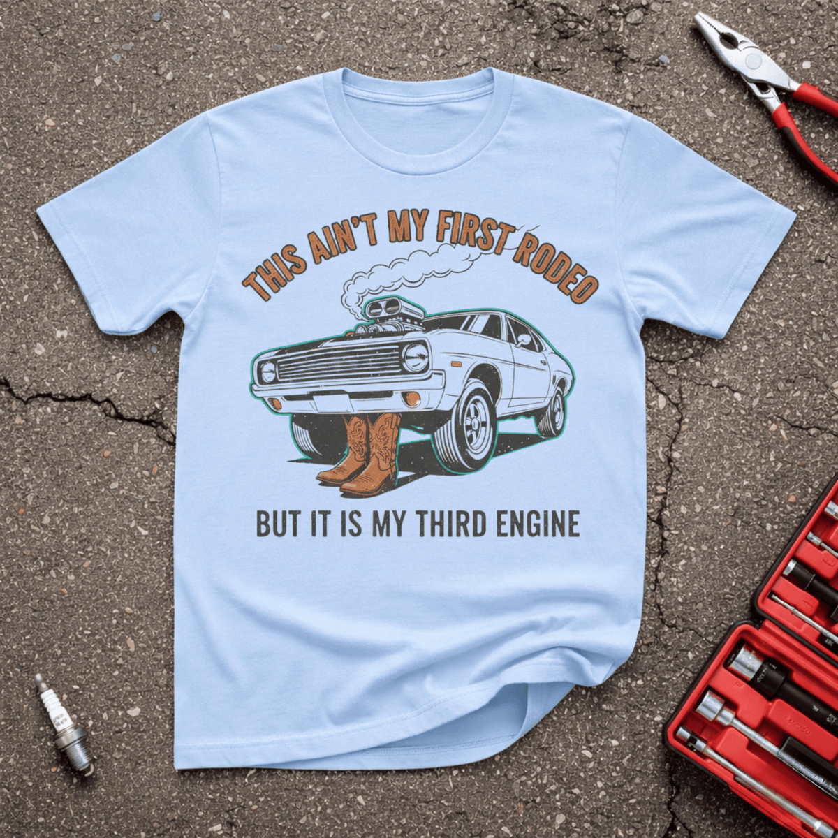 First Rodeo Garage Giggles T-shirt on light blue with classic hot rod, cowboy boots and the words This Ain’t My First Rodeo But It Is My Third Engine.