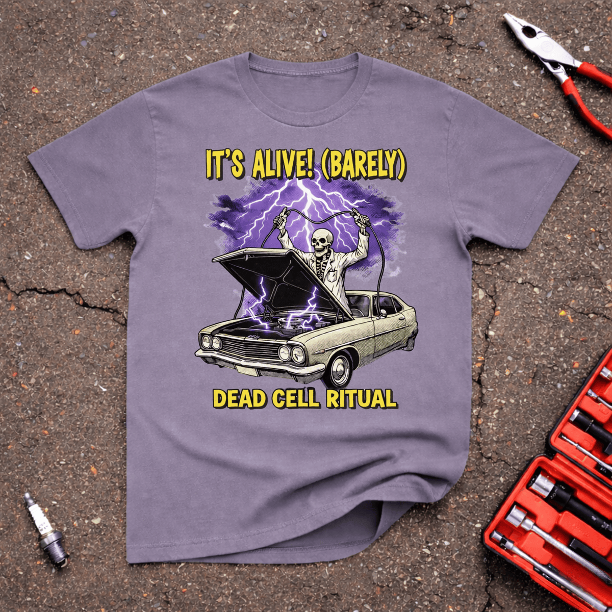 It’s Alive! paragon purple project car humor t-shirt showing a skeleton scientist raising jumper cables over a classic car with the hood open, purple lightning, and Dead Cell Ritual text — GarageGiggles.com automotive apparel.