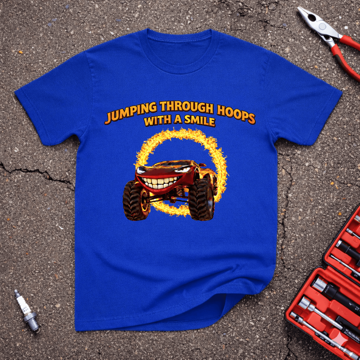 Jumping Through Hoops funny automotive T-shirt featuring a grinning monster vehicle jumping through a flaming hoop on a royal blue shirt.