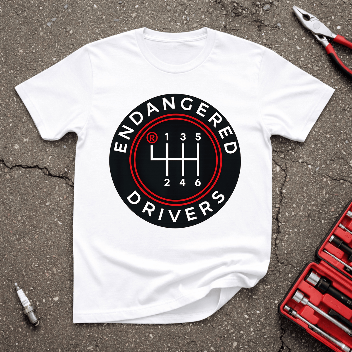Endangered Drivers Garage Giggles T-shirt with six-speed manual shift pattern in black and red on a white shirt.
